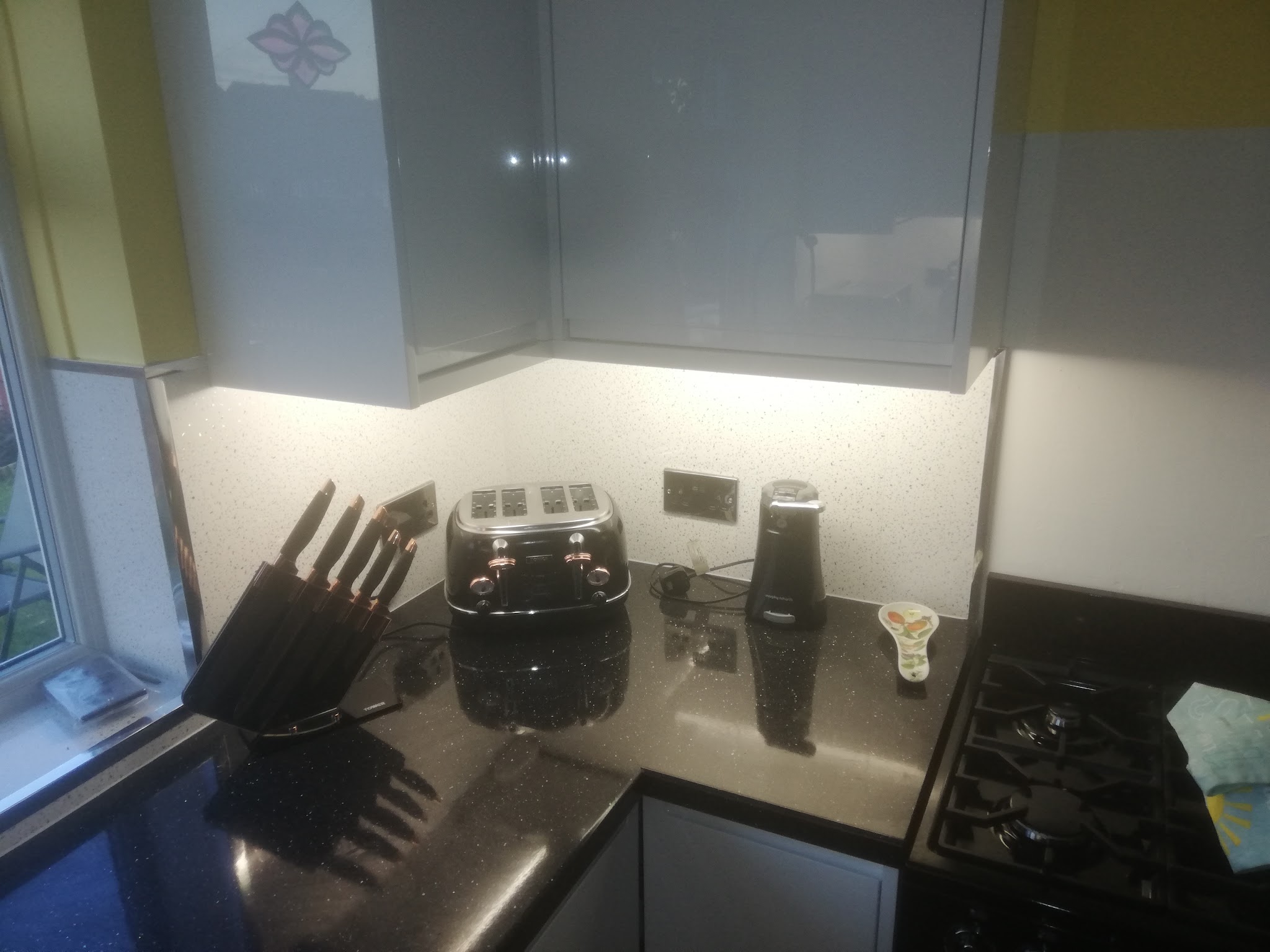 LED lighting under kitchen wall cabinets above a black worktop